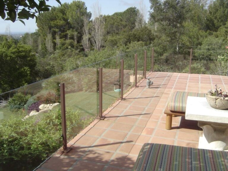 Outdoor patio with glass railing overlooking a landscaped garden, Callender's House Of Glass