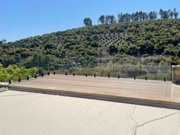 Callender's House Of Glass outdoor glass railing on wooden deck with forested hillside background