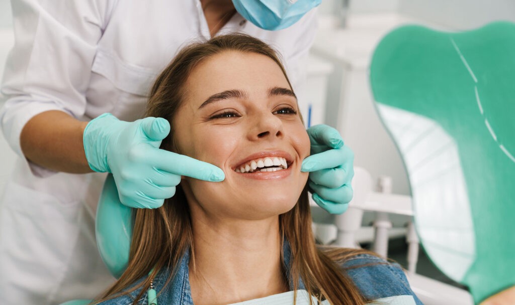 A close-up of a smiling woman's face, with her eyes closed and mouth open, showcasing a clean and healthy smile.