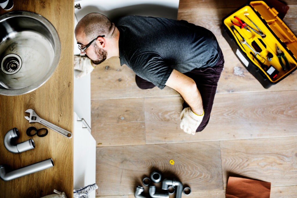 Plumber from R J Carroll & Sons Plumbing installing a pipe under a sink with tools nearby