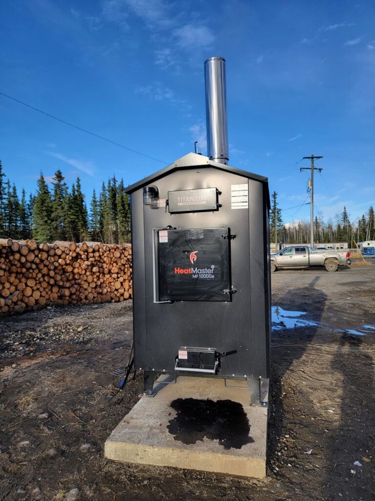 ACS Mechanical Inc. industrial heating unit with chimney and wood storage at outdoor job site