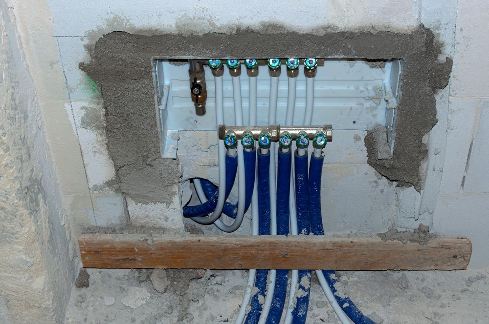 ACS Mechanical Inc. plumbing manifold with blue and white PEX lines in an exposed wall