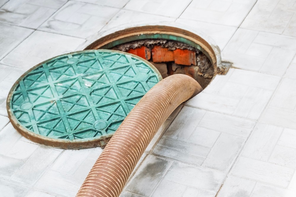 ACs Mechanical Inc sewer drain inspection with vacuum hose and manhole cover on tile floor