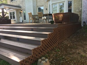 Residential deck with staircase and landscaping in front of a brick home, outdoor seating area