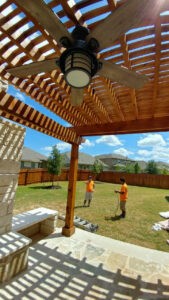 Protractor Roofing crew installs a ceiling fan under wooden porch rafters
