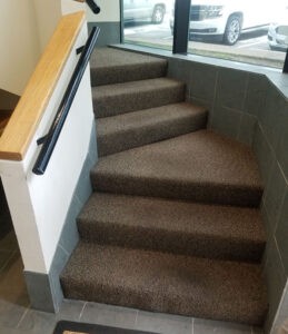 Protractor Roofing—interior carpeted staircase in a modern building entryway