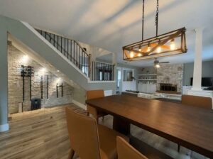 Protractor Roofing interior image featuring a modern living and dining area with exposed ceiling lighting and a stone fireplace wall