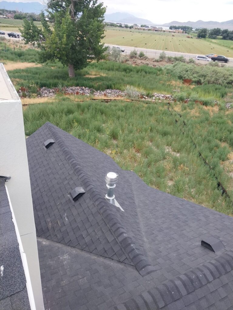 A+ Roofing Services installing or inspecting asphalt shingle roof with vent pipes overlooking a rural landscape